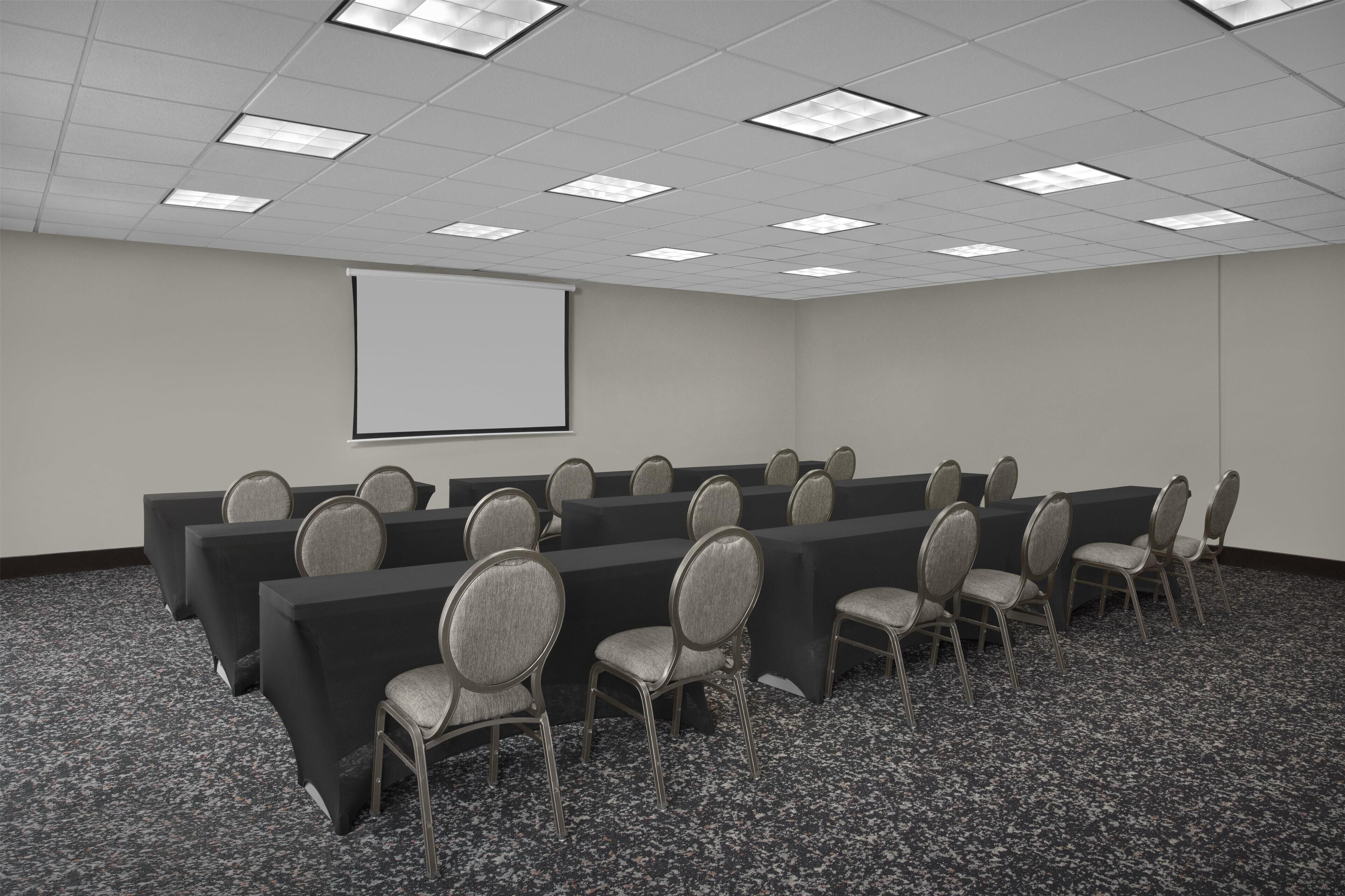 Uma sala de conferências com tela de projetor, fileiras de mesas e cadeiras.