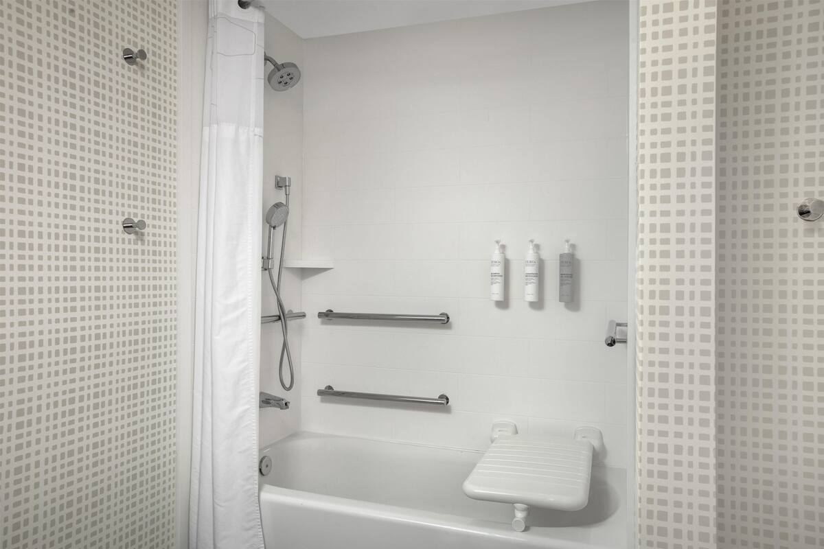 A bathroom with a bathtub, shower, grab bars, and a towel rack.