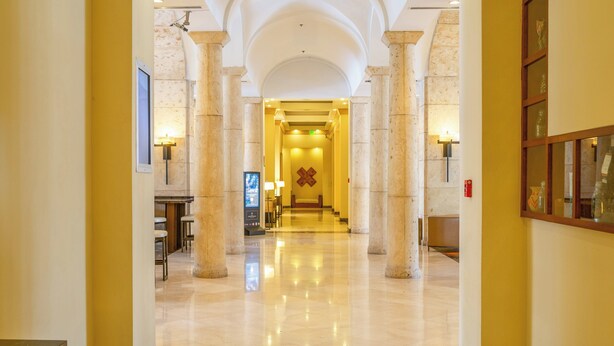 Un vestíbulo de hotel con piso de mármol, columnas y una mesa de recepción.