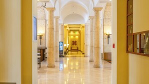 Un vestíbulo de hotel con piso de mármol, columnas y una mesa de recepción.
