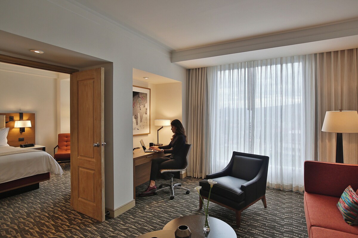 Habitación de hotel con cama, escritorio con computadora portátil, silla, sofá y mesa de centro.