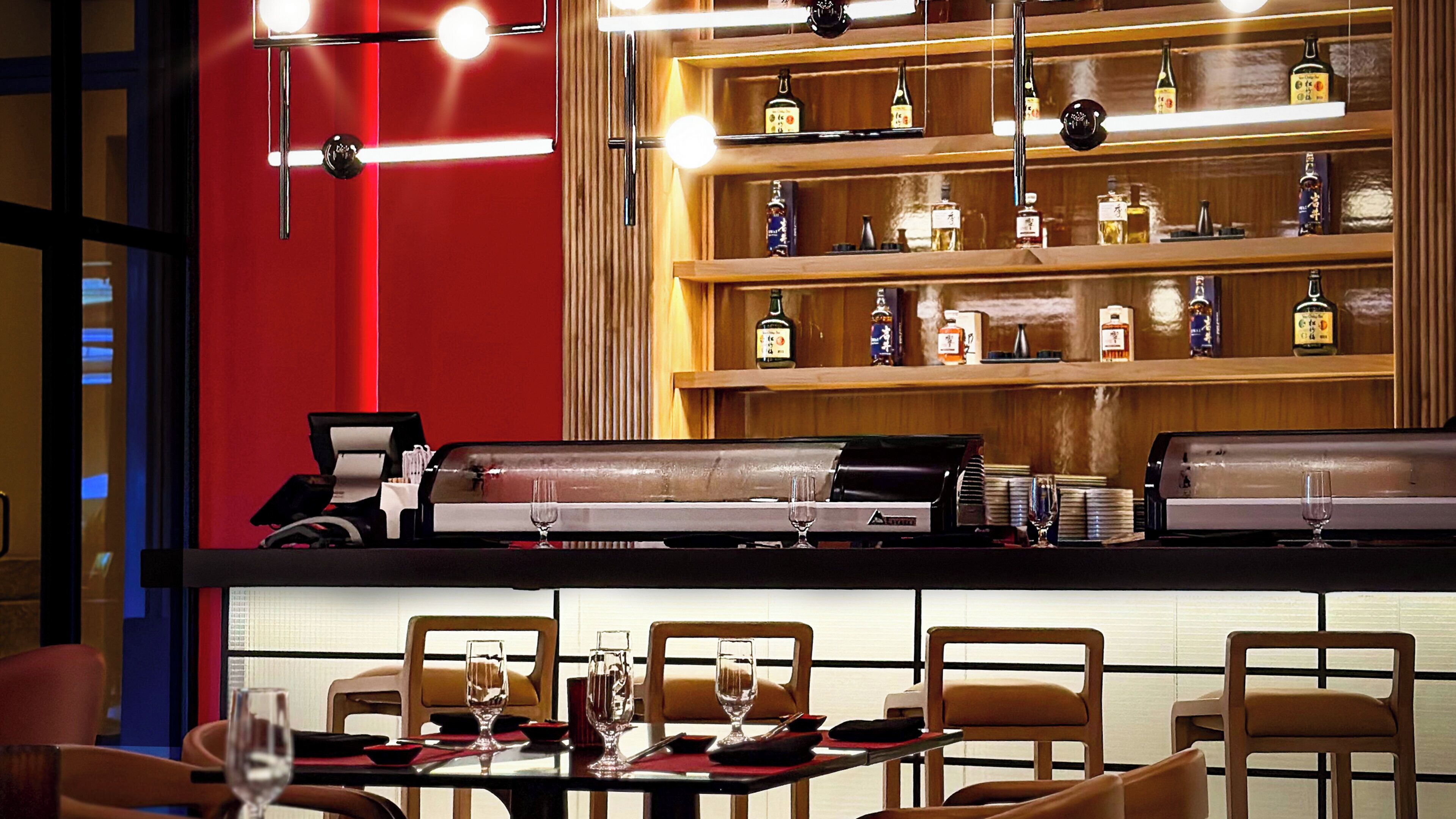 Un espace bar avec un mur rouge, des étagères remplies de bouteilles d’alcool et un comptoir en cuir.