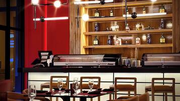Un espace bar avec un mur rouge, des étagères remplies de bouteilles d’alcool et un comptoir en cuir.