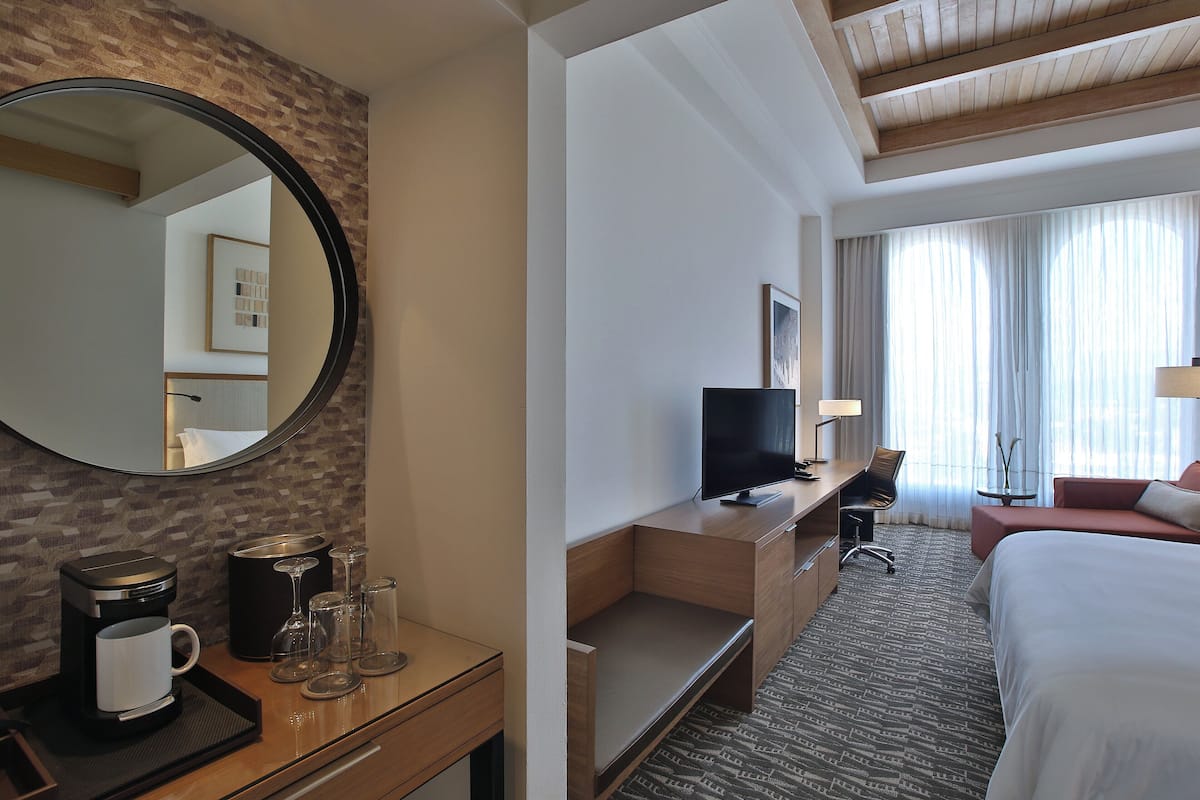 A hotel room with a wooden desk, a television, a bed, and a large mirror.