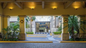Entrada de hotel con un camino pavimentado, palmeras y un letrero que dice "MULTIPLAZA".