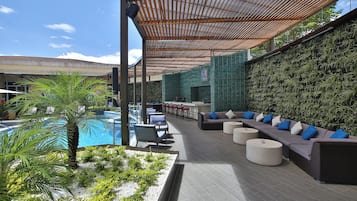 Un área de lounge en la azotea con piscina, asientos exteriores y un muro verde.