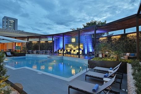 Una piscina al aire libre, sombrillas, sillones reclinables de piscina