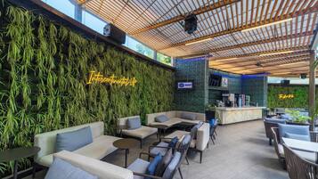An indoor seating area with sofas and tables, a green wall with hanging plants, and a bar area.