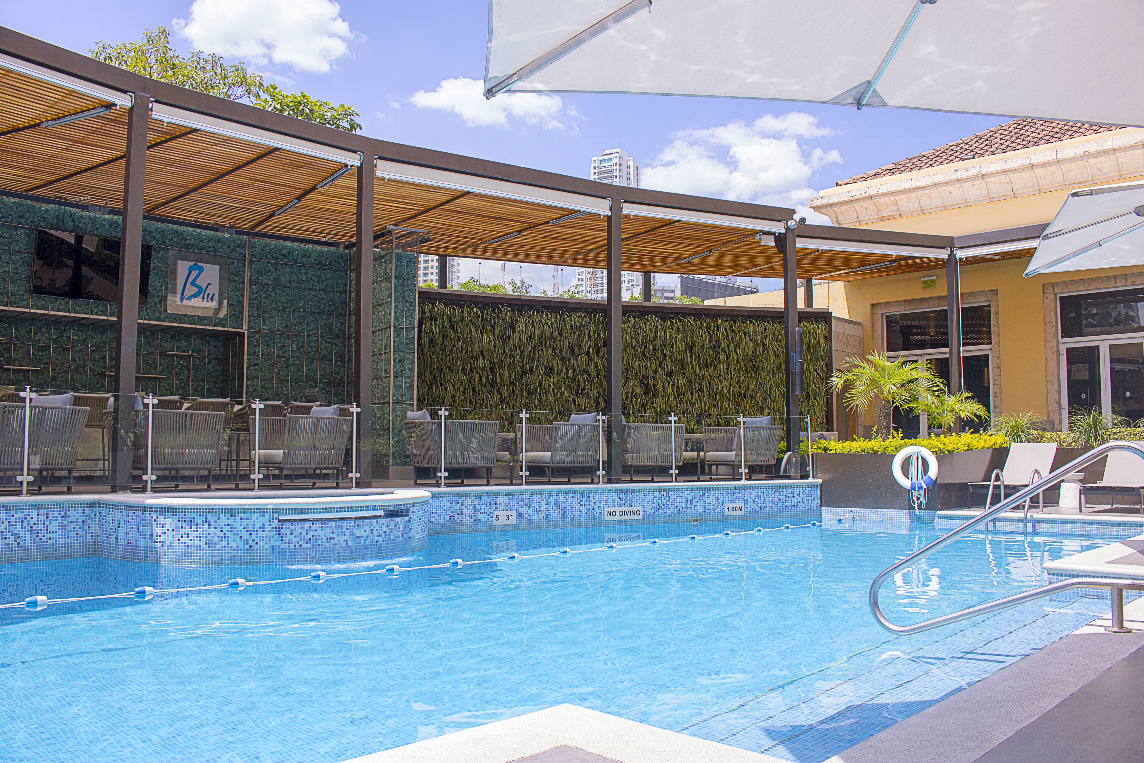 A swimming pool with a tiled edge, a no diving sign, and a shaded area with chairs.