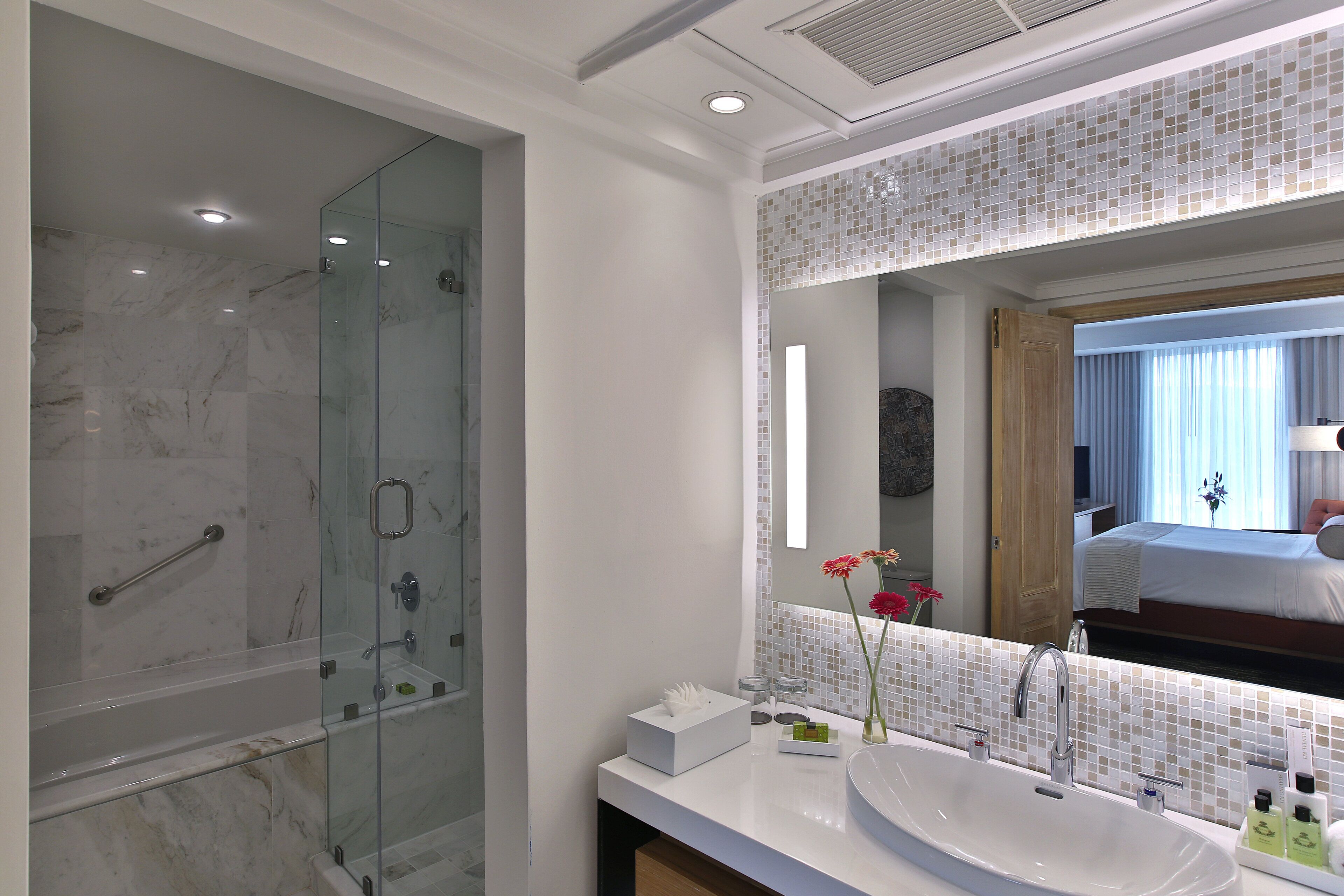 Un baño moderno con ducha de vidrio, un espejo grande y un lavamanos blanco.