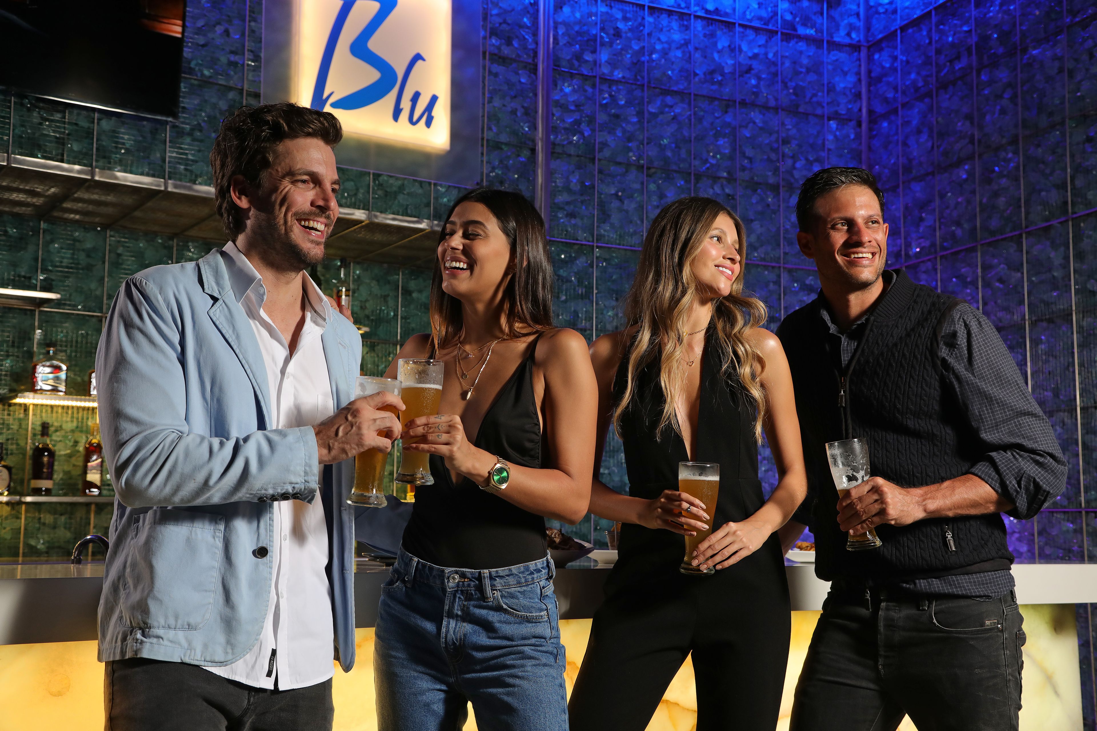 A group of people standing in a bar area with a large illuminated sign in the background.