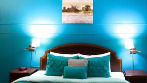 A bedroom with a teal-colored bedspread, a wooden headboard, and two bedside lamps. - Gables Inn  (Coral Gables)