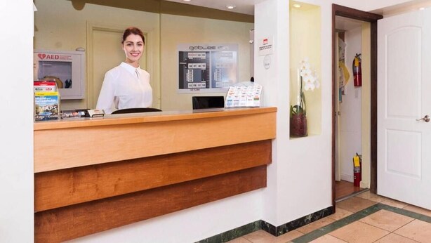 A reception desk with a receptionist, a computer, and informational brochures. - Gables Inn  (Coral Gables)