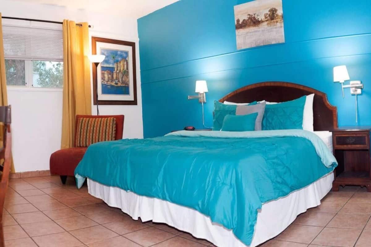 A bedroom with a large bed, a chair, a nightstand, and a wall-mounted lamp.