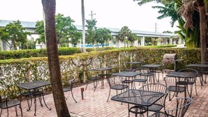 An outdoor patio area with multiple tables and chairs, surrounded by hedges and trees. - Gables Inn  (Coral Gables)