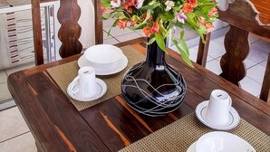 A dining area with a table set for two, a vase of flowers, and a television in the background. - Hotel Vallartasol (Puerto Vallarta)