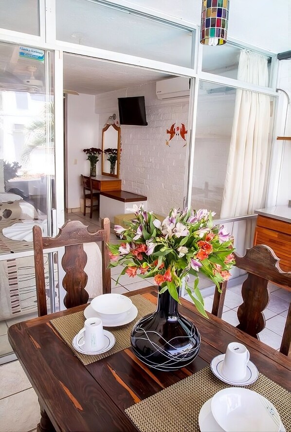 Un coin repas avec une table dressée pour deux personnes, un vase de fleurs et un téléviseur en arrière-plan.