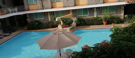 A swimming pool with a lounge area, surrounded by potted plants and a building with balconies.