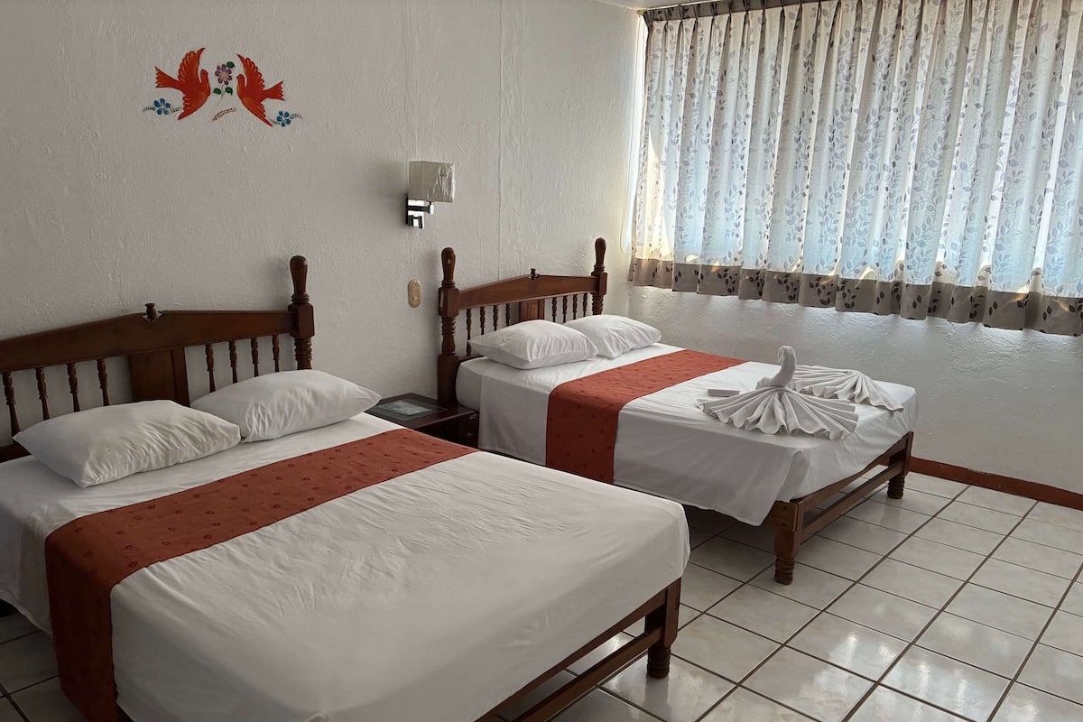 Een hotelkamer met twee houten bedden, witte beddengoed en een rode plaid.
