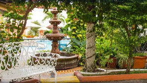 A fountain, a white wrought-iron bench, and potted plants in a garden area. - Hotel Vallartasol (Puerto Vallarta)