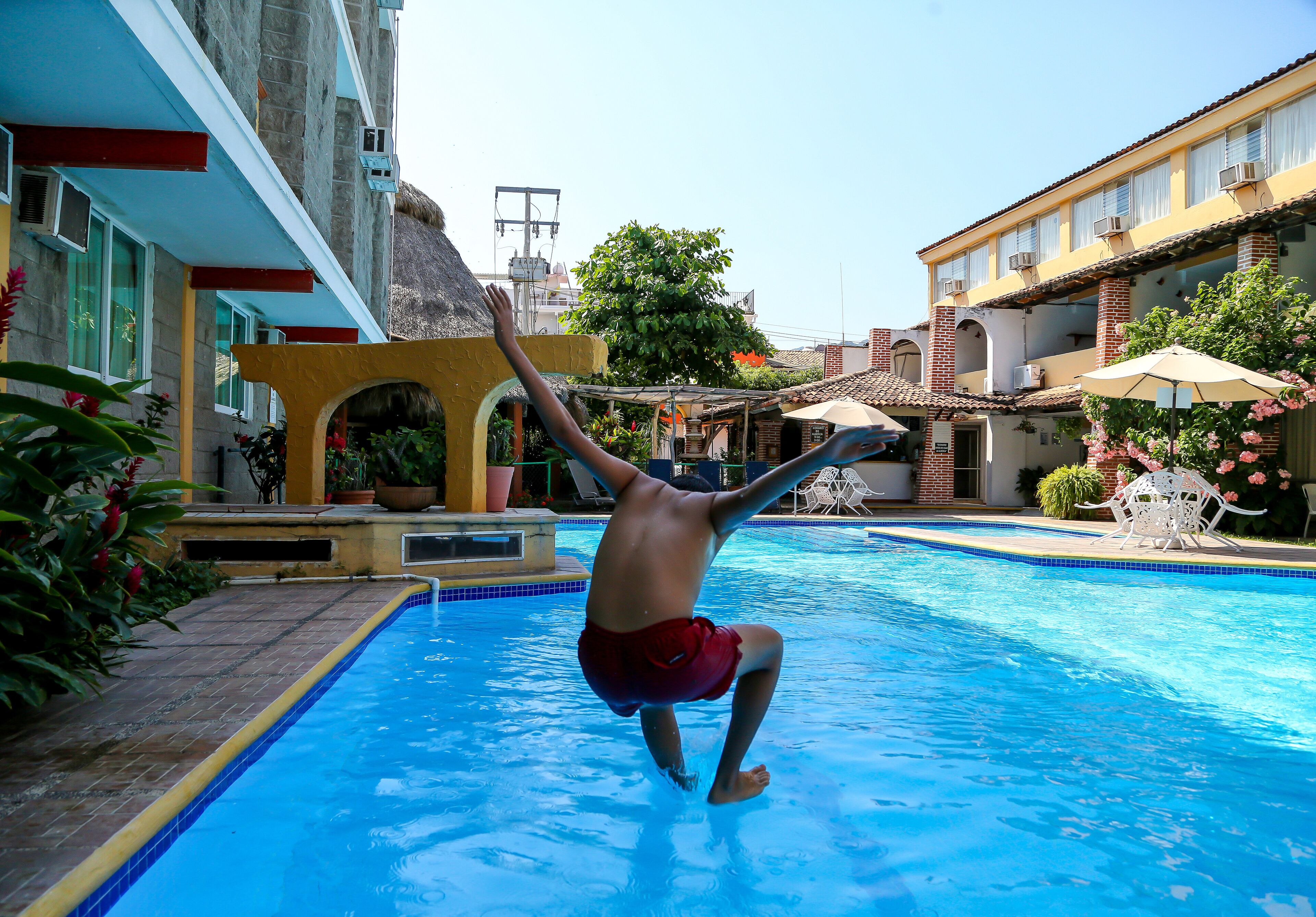 A man jumping into a swimming pool surrounded by buildings and plants.