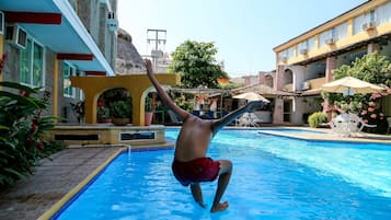 A man jumping into a swimming pool surrounded by buildings and plants.