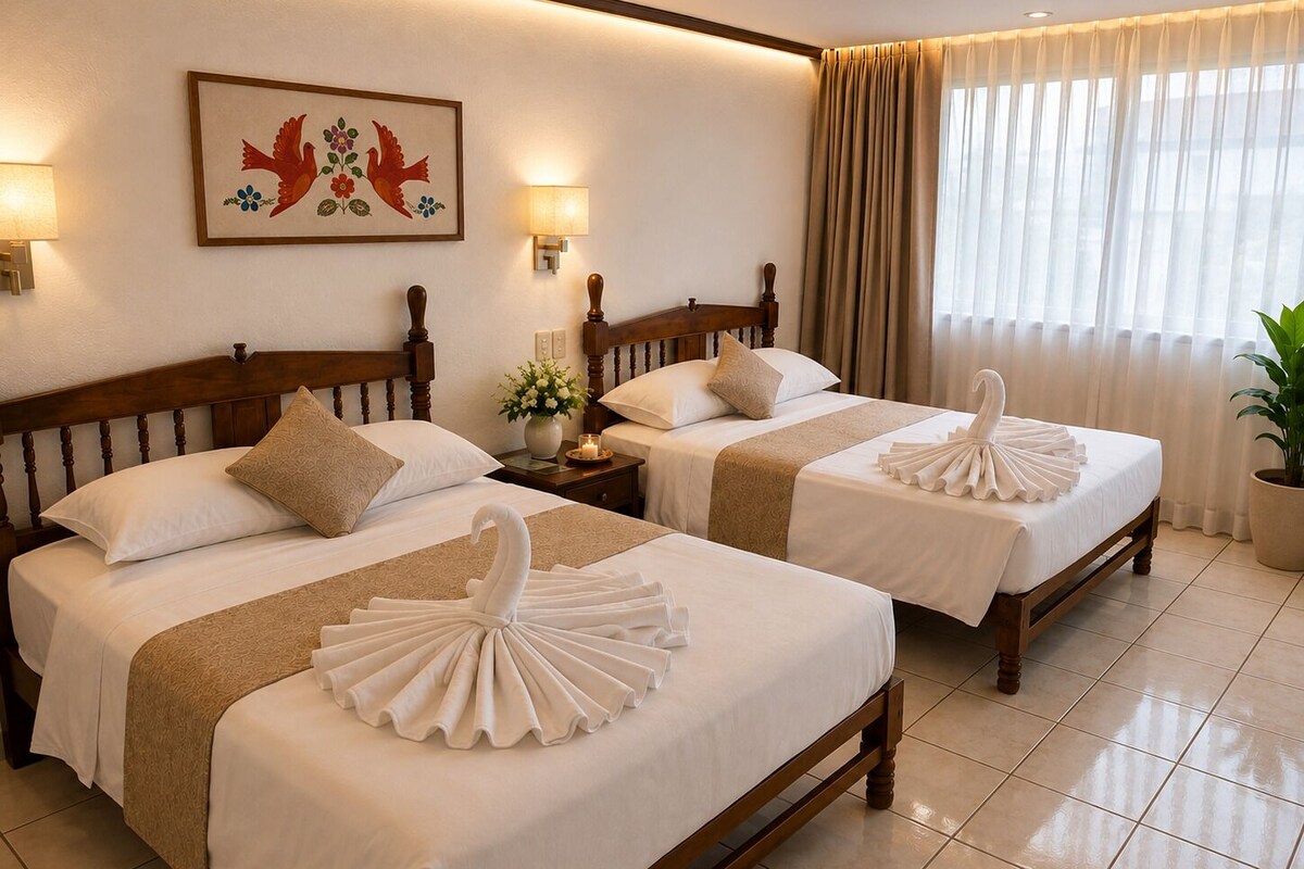 A hotel room with two beds, each with a swan-shaped towel, a wooden headboard, a wall-mounted lamp, and a floral painting.