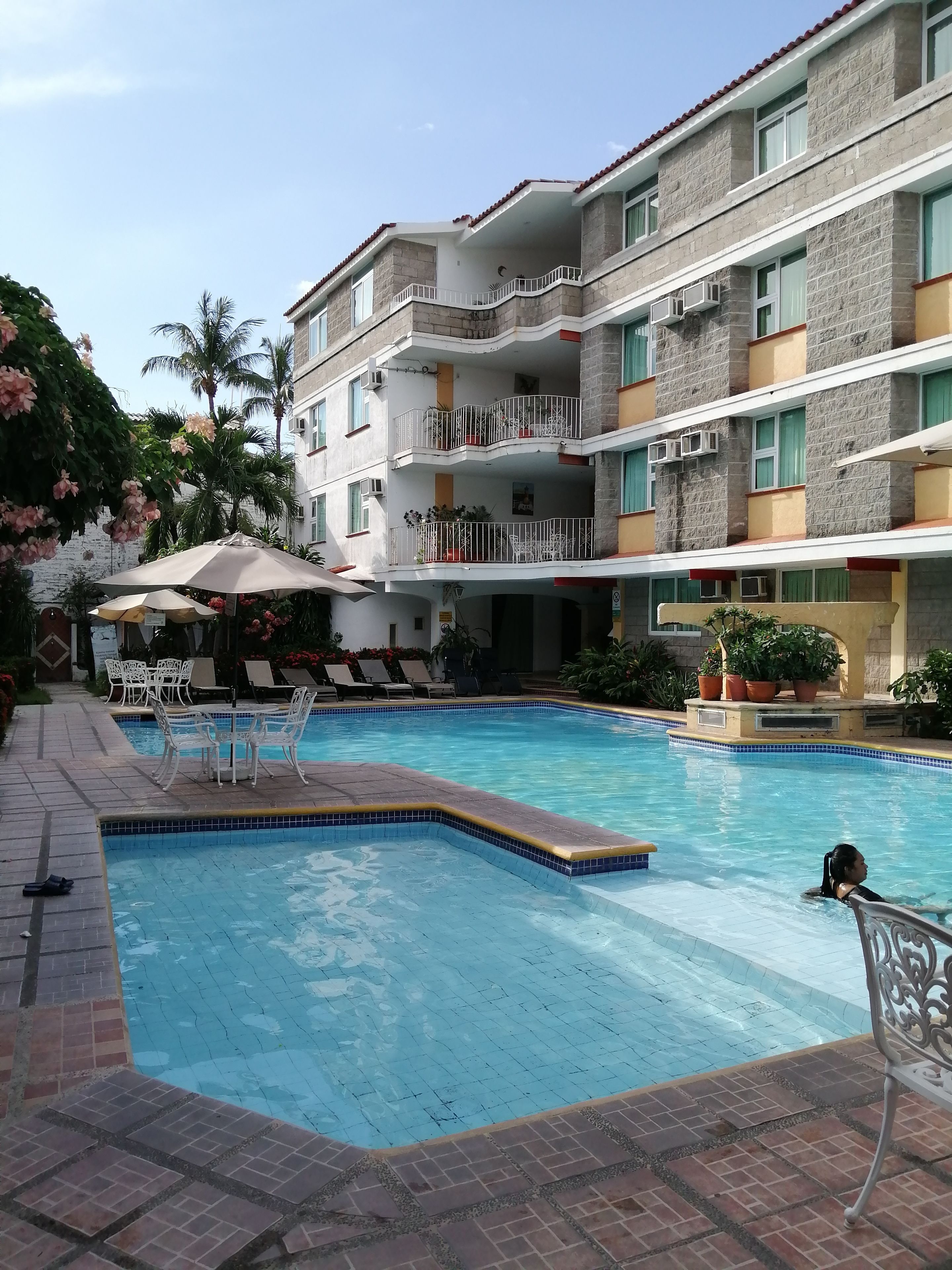A swimming pool with tiled edges, surrounded by lounge chairs and umbrellas.