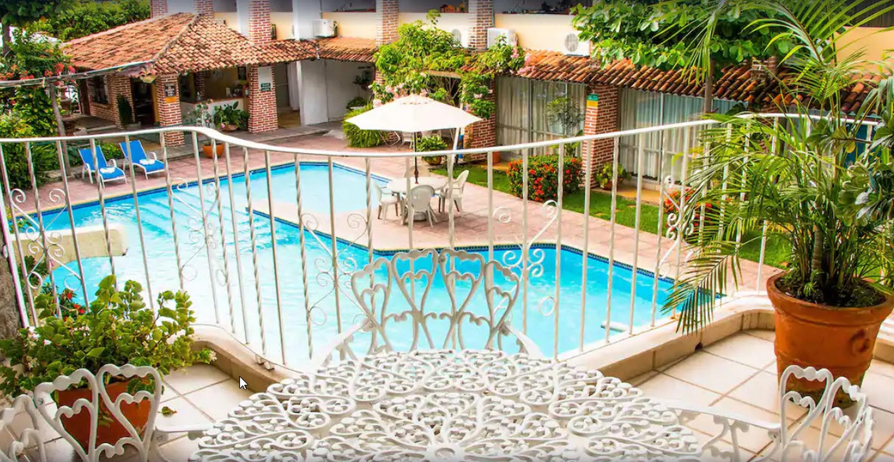 A rooftop pool area with a tiled roof, a pool surrounded by a white fence, and potted plants.