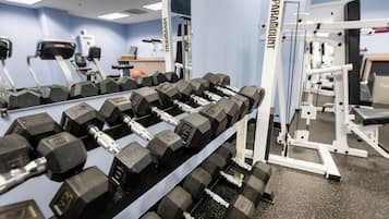 A gym with multiple rows of dumbbells, exercise machines, and a wall-mounted mirror.
