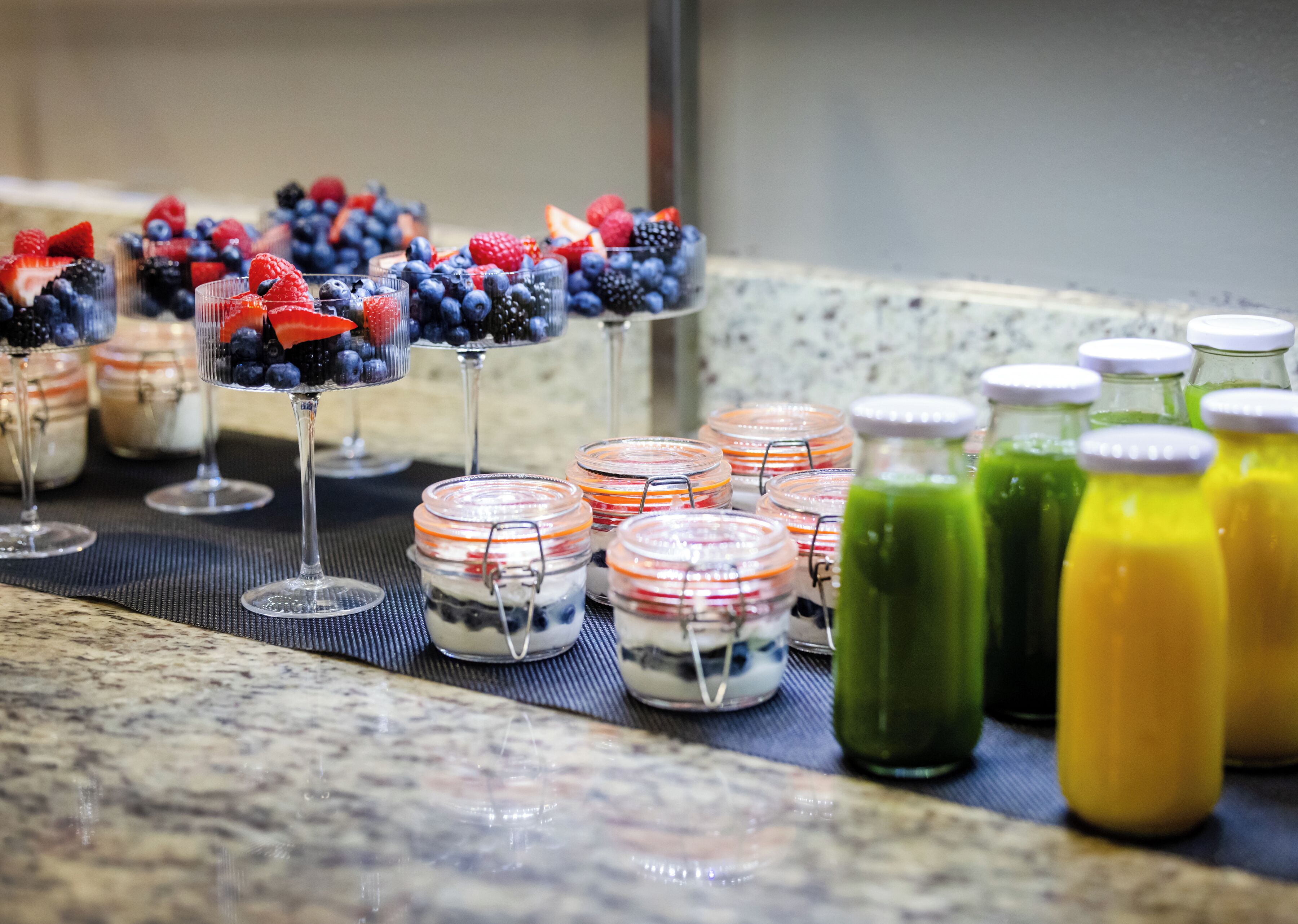 Une table de buffet proposant divers plats, notamment des parfaits aux fruits et des smoothies colorés.