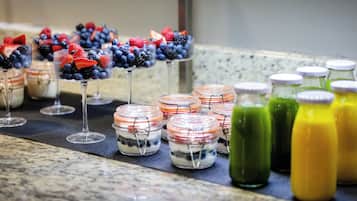 Une table de buffet proposant divers plats, notamment des parfaits aux fruits et des smoothies colorés.