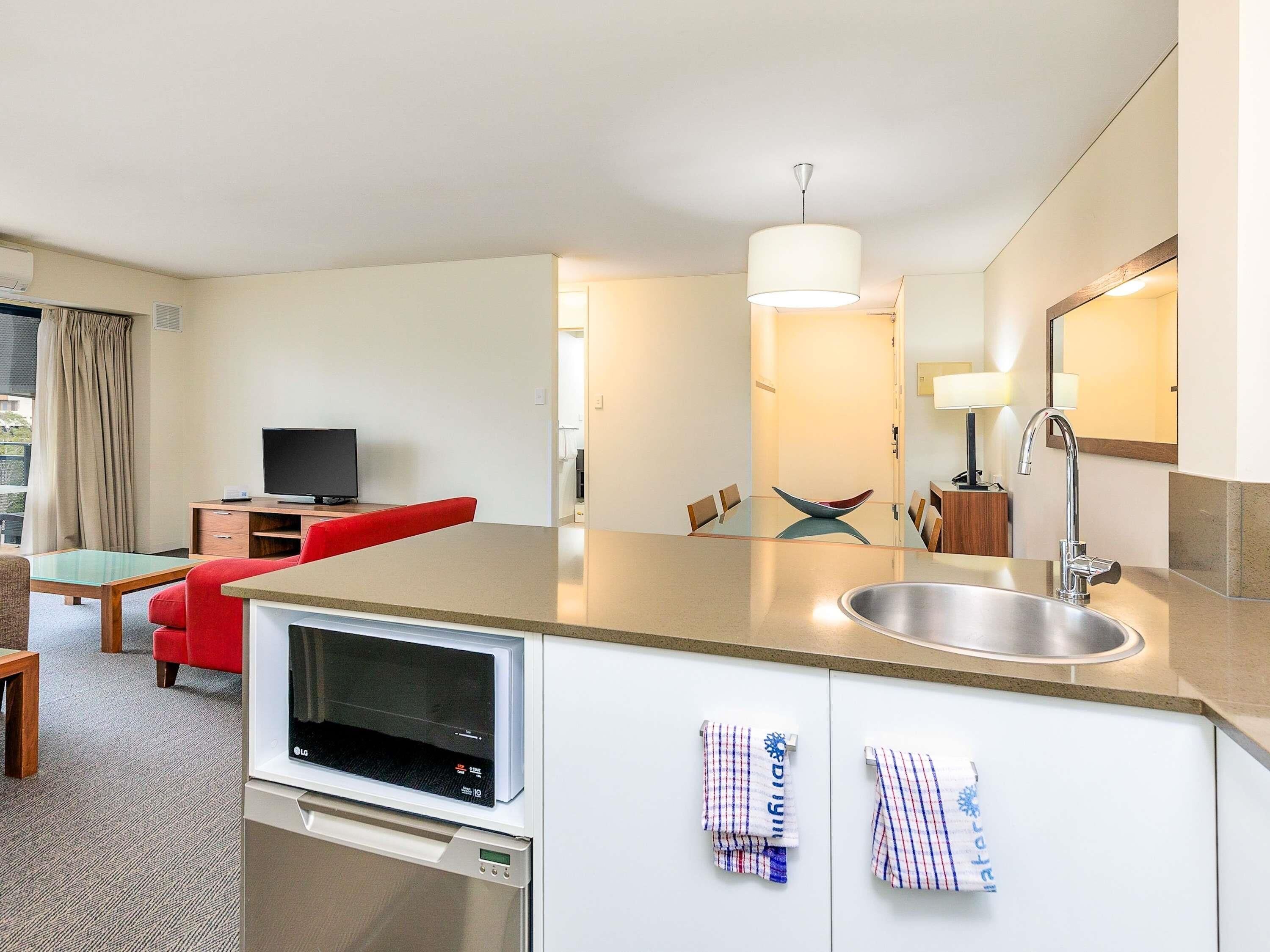 A hotel room with a TV, red sofa, dining table, microwave, sink, and a large mirror.