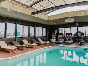 An indoor swimming pool with lounge chairs, exercise equipment, and a sign indicating pool depth.
