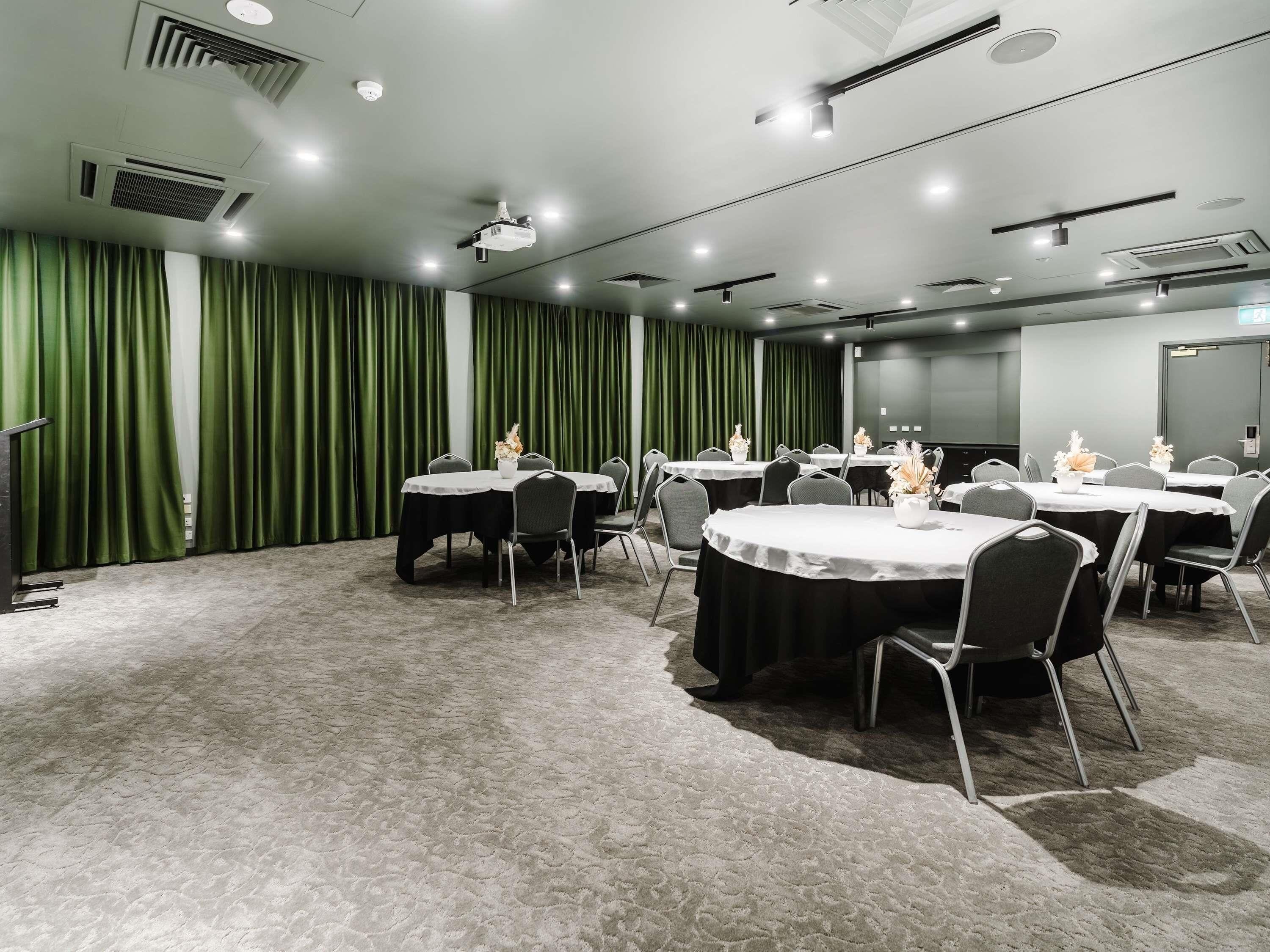 A conference room with round tables, chairs, and green curtains.