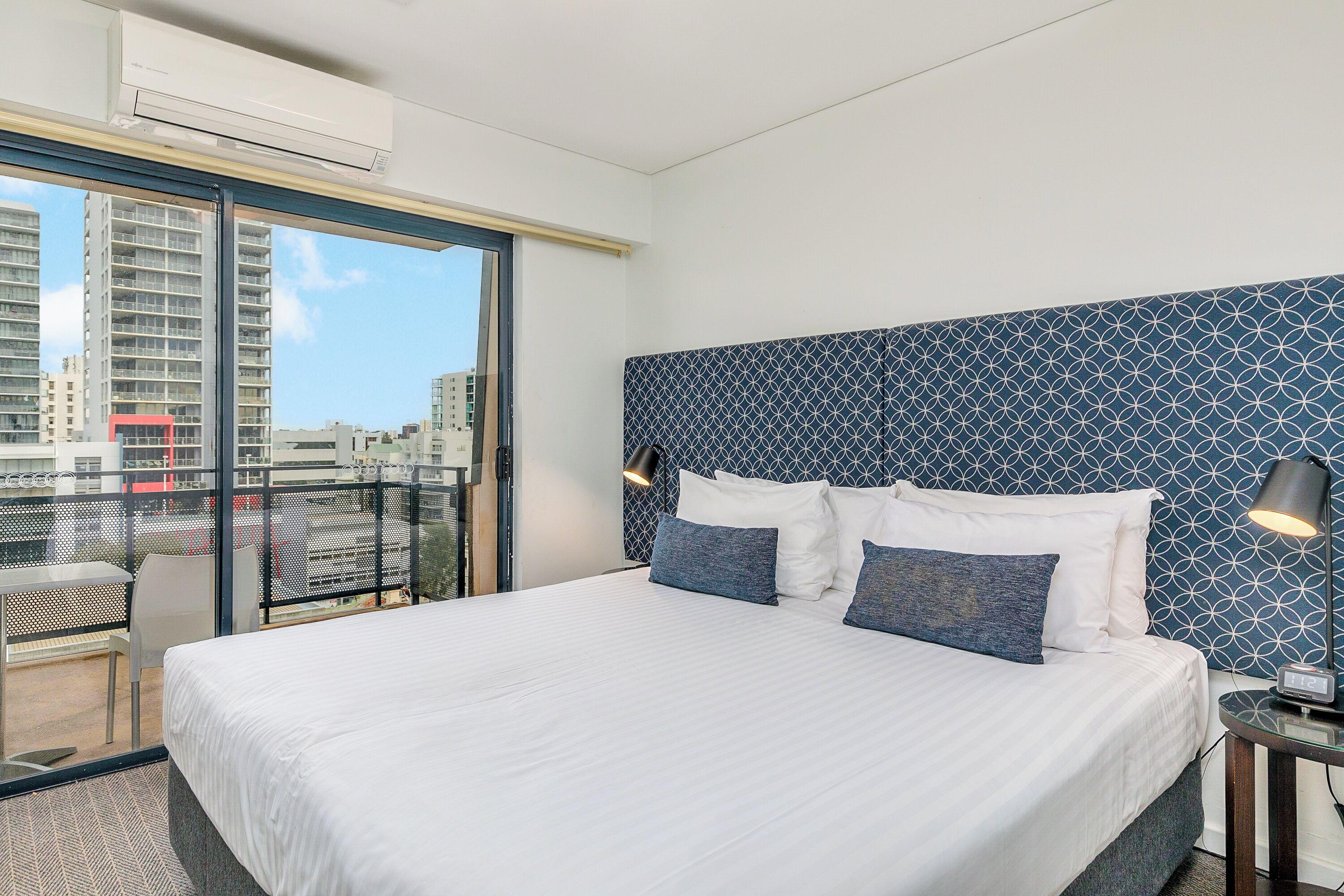 Une chambre d’hôtel avec un grand lit, une vue sur la ville depuis un balcon et une tête de lit décorée.