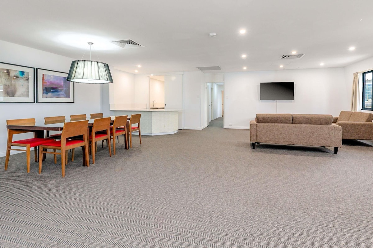 A modern living room with a dining area, a kitchen, and a TV mounted on the wall.