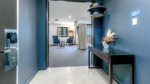 A hallway with a dark blue wall, a wooden console table with a vase, and a door leading to a room with a dining area. - Mantra on Hay Perth (East Perth)