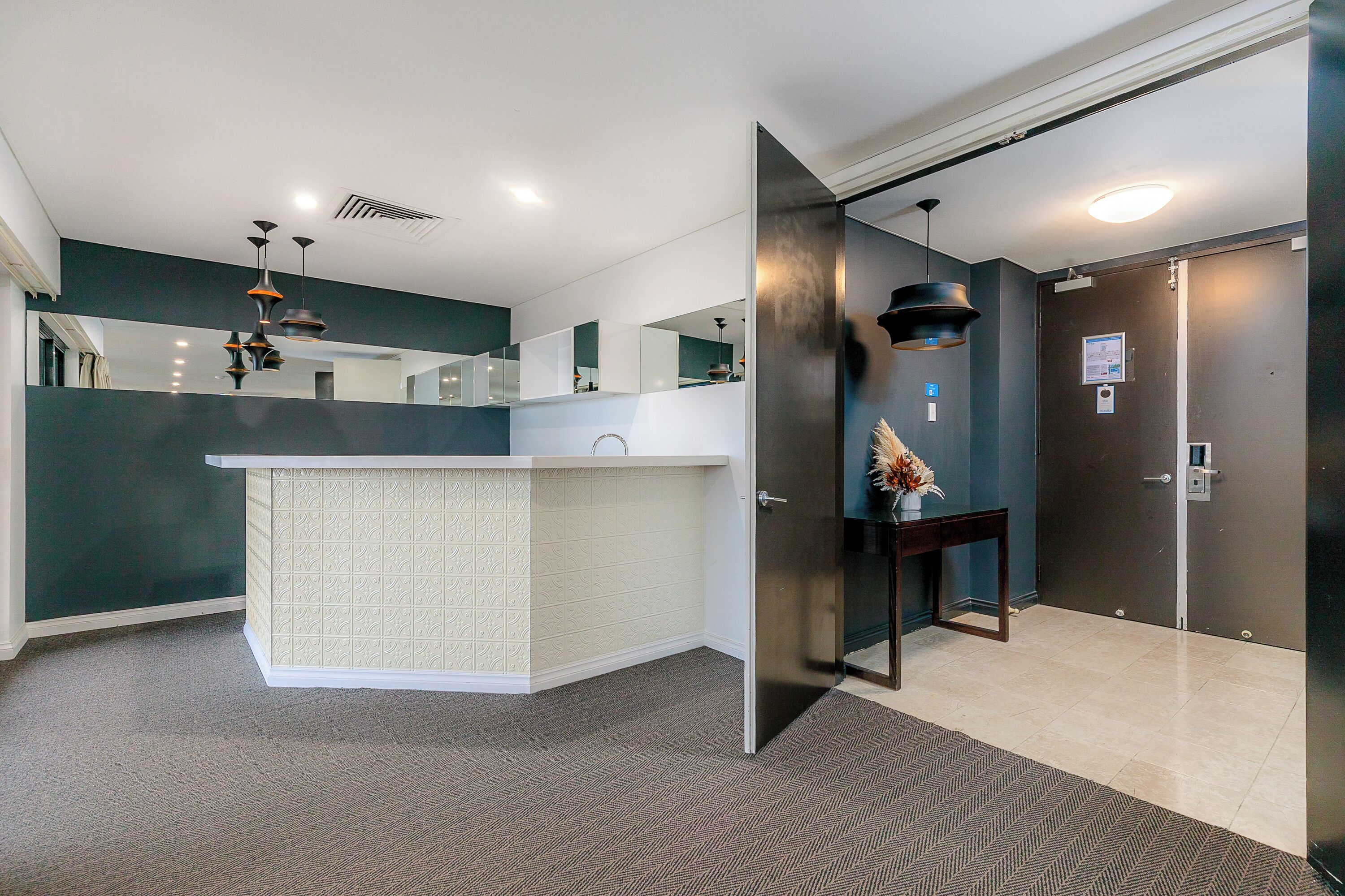Un vestíbul d'hotel modern amb una recepció, una porta fosca i una catifes amb disseny.