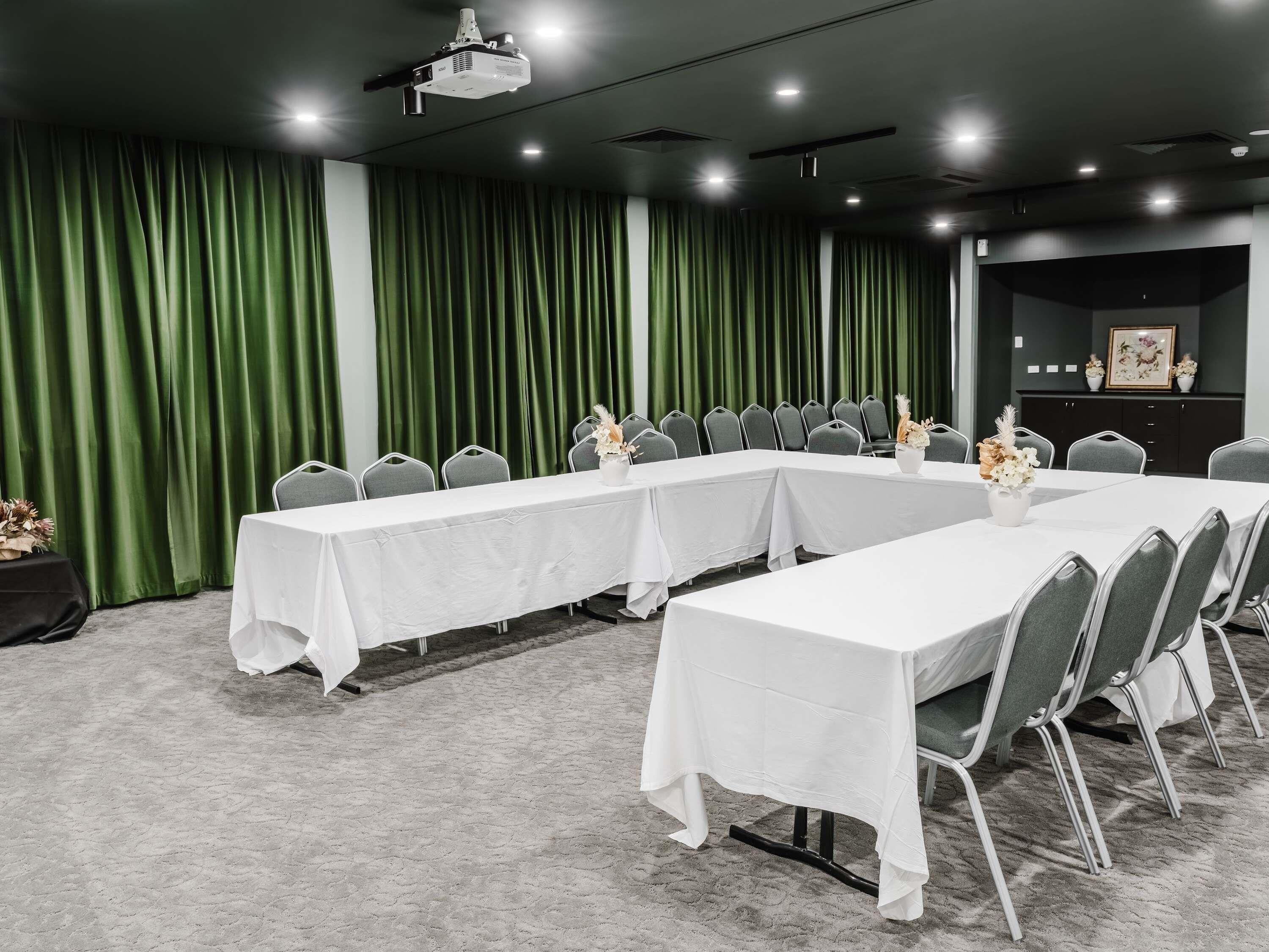 A conference room with a long table, chairs, a projector, and green curtains.