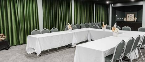 A conference room with a long table, chairs, a projector, and green curtains.