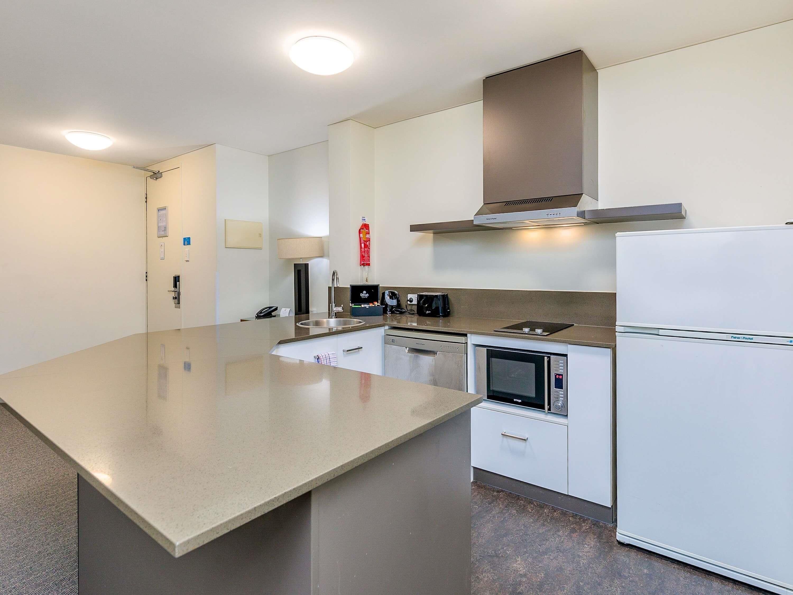 A modern kitchen with a large island, built-in oven, microwave, and a refrigerator.
