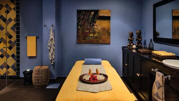 A spa room with a massage table, towels, a painting, and a dark wooden cabinet with a mirror.