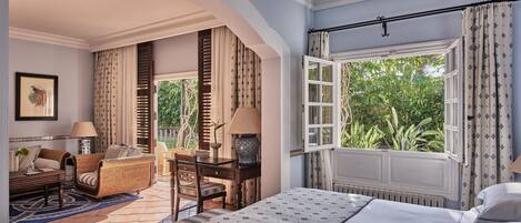 Une chambre avec un grand lit, un bureau, une chaise et une fenêtre donnant sur un paysage verdoyant.