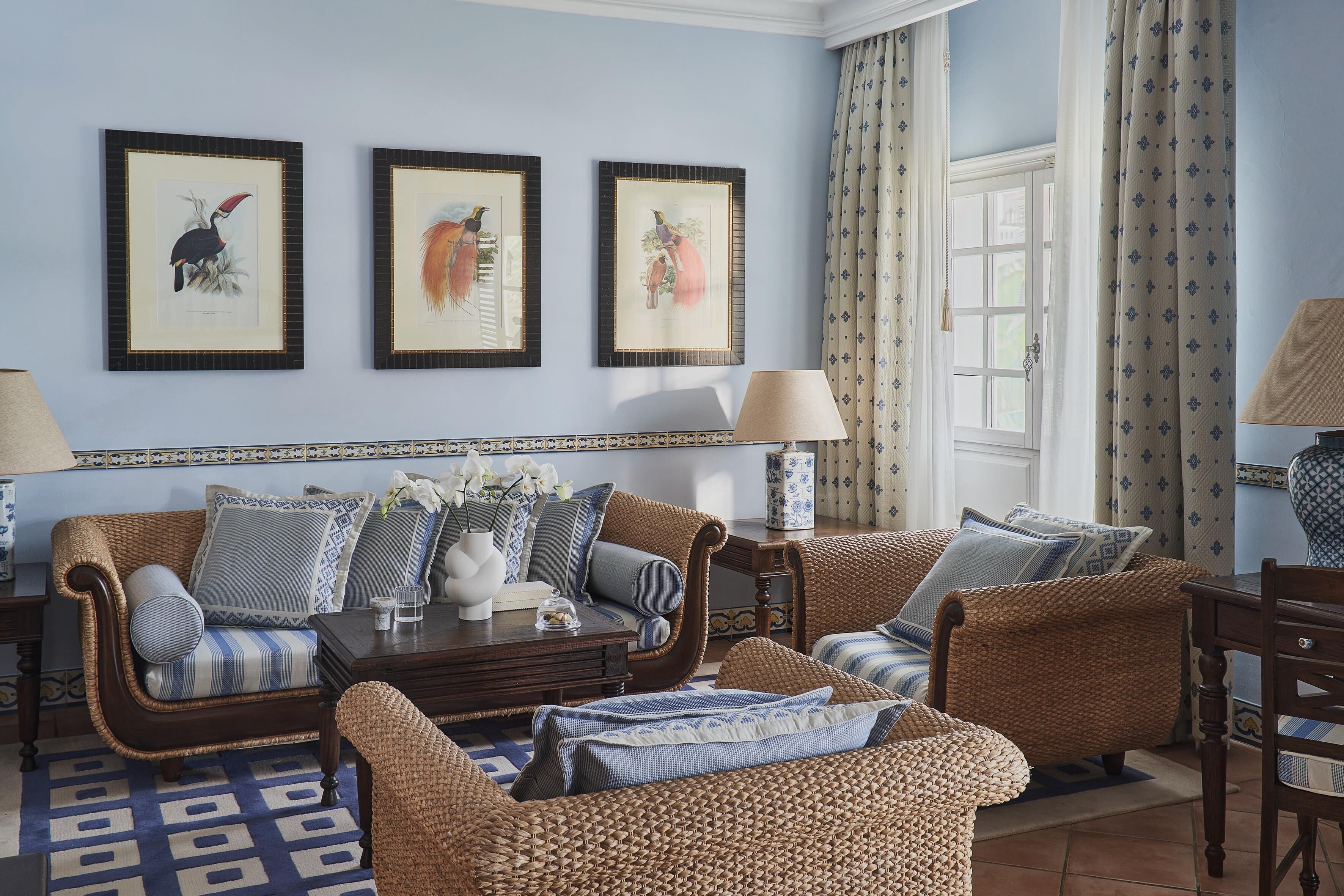 A living room with wicker furniture, framed artwork on the wall, and a view of the outdoors.