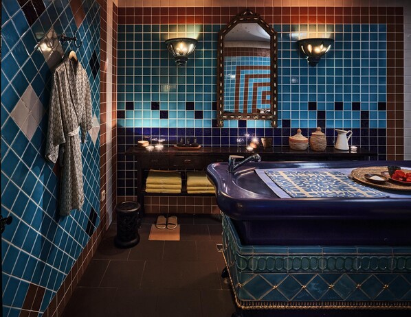 Um banheiro com parede em azulejos azuis, pia com espelho e banheira azul.