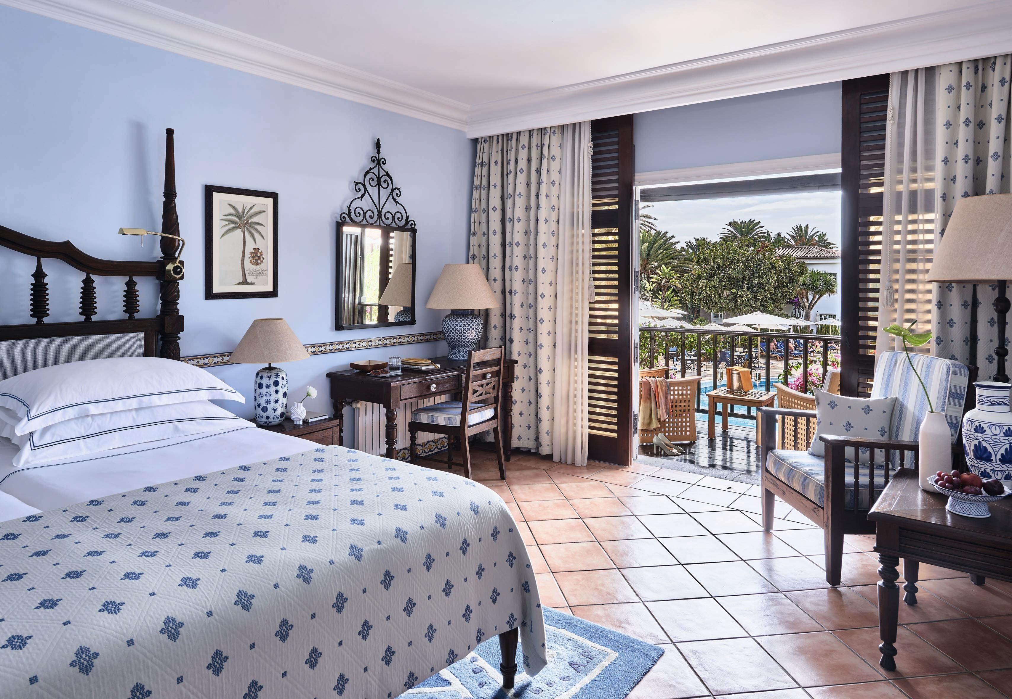 Una habitación de hotel con cama, escritorio, silla y balcón con vista a la piscina.