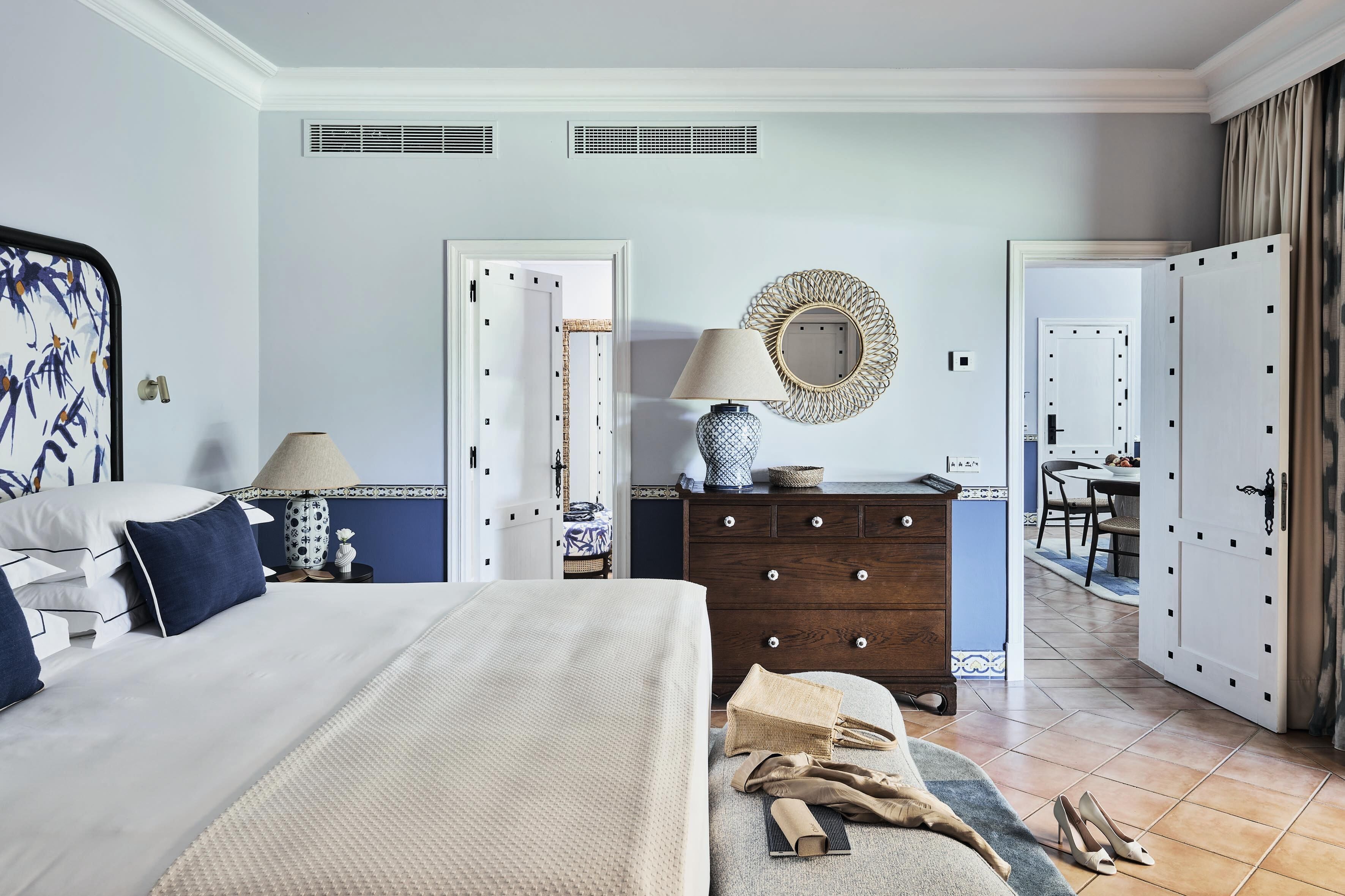 Ein Hotelzimmer mit Bett, Kommode, Lampe, Spiegel und Blick auf den Speisesaal.