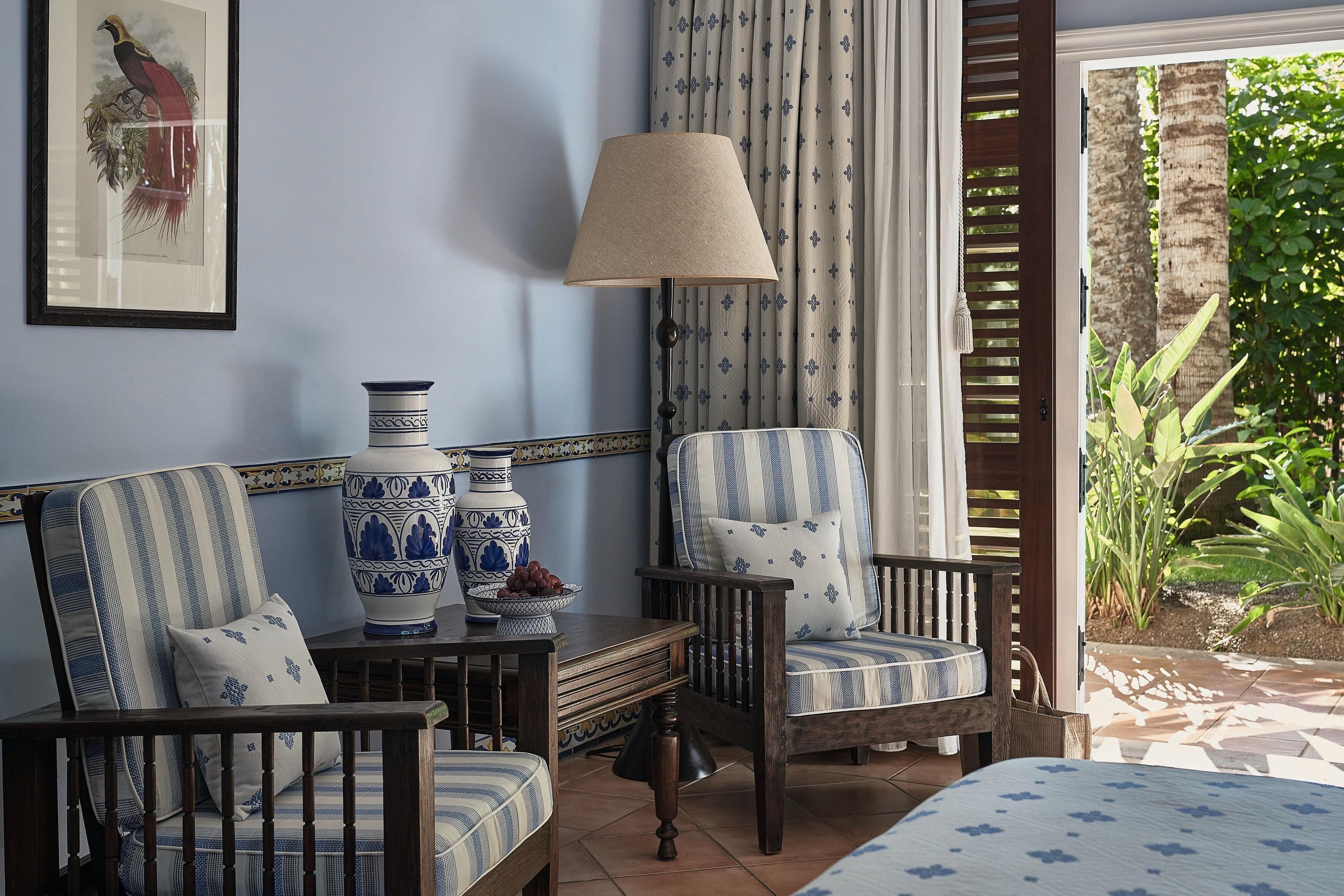 A room with a blue and white striped armchair, a wooden table with a vase and a bowl, and a lamp.