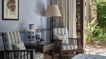 A room with a blue and white striped armchair, a wooden table with a vase and a bowl, and a lamp.